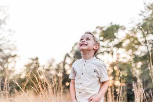 young toddler boy in H and M clothing in a field running and smiling at the sky